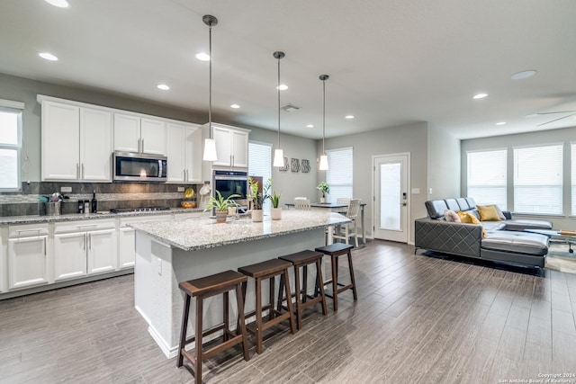 7604 Pecos Rdg, Boerne, TX 78015 - kitchen featuring appliances with stainless steel finishes, backsplash, wood finished floors, an island with sink, and a kitchen bar