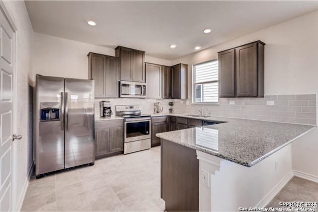 3951 Gentle Mdw, New Braunfels, TX 78130 - kitchen with appliances with stainless steel finishes, a peninsula, dark brown cabinetry, light stone counters, and decorative backsplash
