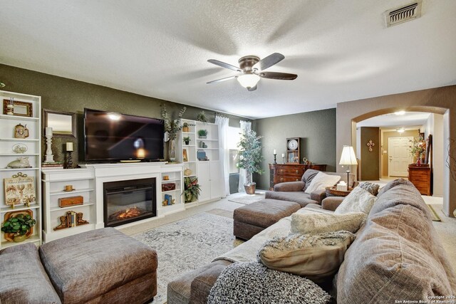 181 Foxglove, Cibolo, TX 78108 - carpeted living room with a ceiling fan, arched walkways, a glass covered fireplace, and a textured ceiling