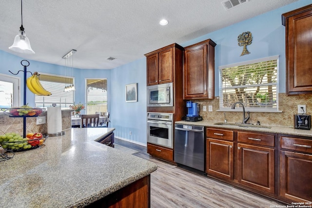 12535 Panola Way, San Antonio, TX 78253 - kitchen with stainless steel appliances, a sink, a textured ceiling, light wood finished floors, and decorative backsplash