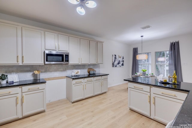 12031 Wellstone, San Antonio, TX 78249 - kitchen featuring stainless steel microwave, decorative backsplash, light wood finished floors, hanging light fixtures, and dark stone countertops