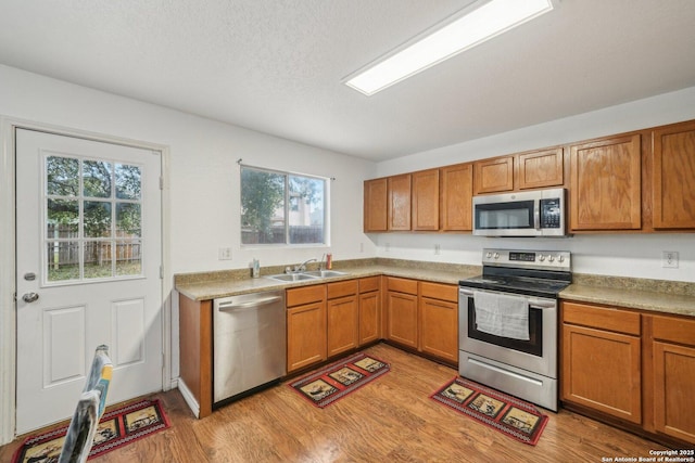 5815 Trent, San Antonio, TX 78249 - kitchen with stainless steel appliances, a sink, light wood-style floors, brown cabinets, and a textured ceiling