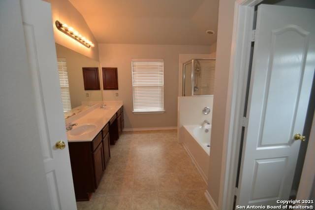 807 Maltese Gdn, San Antonio, TX 78260 - bathroom featuring vaulted ceiling, double vanity, a bath, a shower with door, and baseboards
