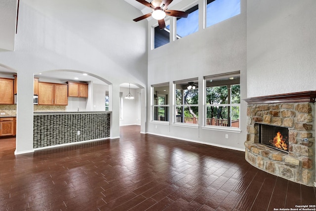 25511 Willard Path, San Antonio, TX 78261 - unfurnished living room with ceiling fan, a fireplace, arched walkways, wood finished floors, and a towering ceiling