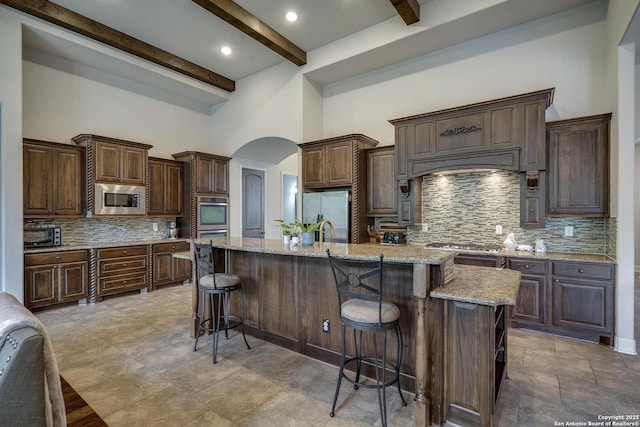 26358 Tawny Way, Boerne, TX 78015 - kitchen featuring appliances with stainless steel finishes, beamed ceiling, arched walkways, backsplash, and a kitchen bar