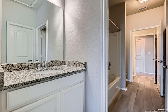 13908 Lazada, San Antonio, TX 78245 - bathroom featuring vanity, wood finished floors,  shower combination, and a textured wall