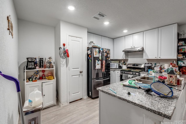 10827 Hernando Ct, Converse, TX 78109 - kitchen featuring freestanding refrigerator, under cabinet range hood, stainless steel gas range, light wood-style floors, and white cabinets