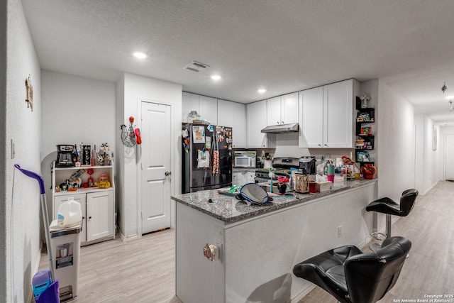 10827 Hernando Ct, Converse, TX 78109 - kitchen featuring freestanding refrigerator, stainless steel stove, light wood-type flooring, under cabinet range hood, and white cabinets