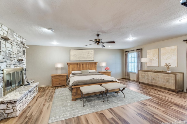 10745 Rosemar Ln, Adkins, TX 78101 - bedroom with wood finished floors, a textured ceiling, a fireplace, baseboards, and ceiling fan