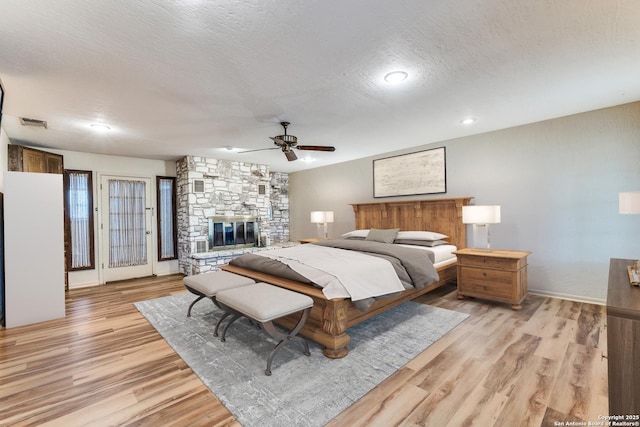 10745 Rosemar Ln, Adkins, TX 78101 - bedroom featuring light wood-style floors, a fireplace, baseboards, a textured ceiling, and ceiling fan