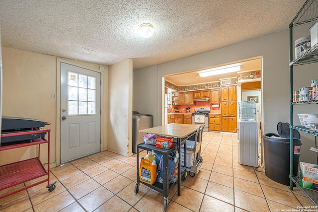 3211 Hatton, San Antonio, TX 78237 - kitchen with stainless steel stove, washer / dryer, brown cabinetry, light tile patterned floors, and a textured ceiling