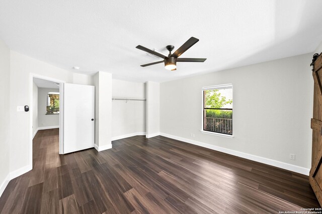 15831 Colton Wl, San Antonio, TX 78247 - unfurnished bedroom featuring a barn door, dark wood-type flooring, a closet, baseboards, and a ceiling fan