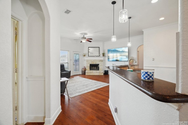 7027 Laura Hts, Schertz, TX 78154 - kitchen featuring arched walkways, a fireplace, dark countertops, a ceiling fan, and crown molding