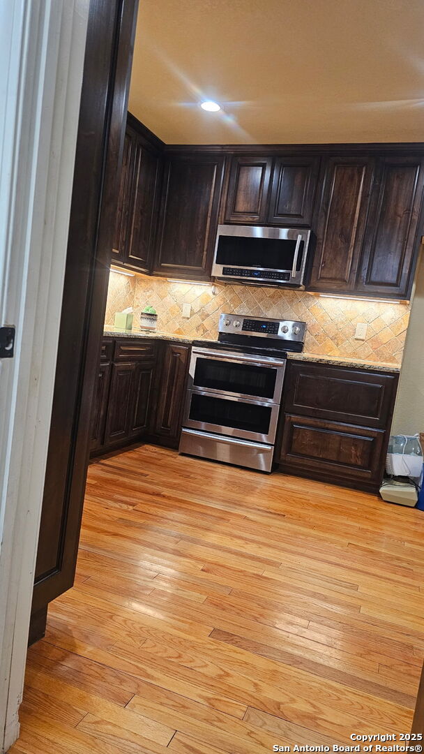 218 E Antonio, Uvalde, TX 78801 - kitchen featuring stainless steel appliances, light wood-type flooring, dark brown cabinetry, backsplash, and light stone counters