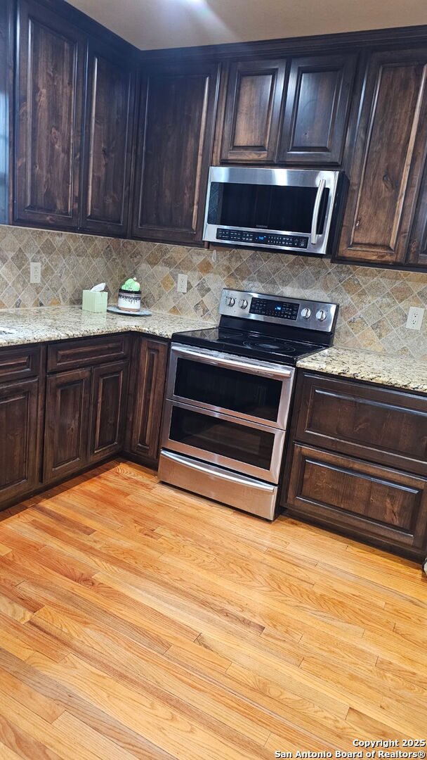 218 E Antonio, Uvalde, TX 78801 - kitchen with appliances with stainless steel finishes, backsplash, dark brown cabinets, light stone countertops, and light wood-style floors