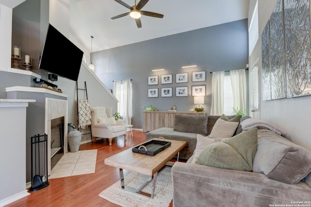 6039 Woodway Ct, San Antonio, TX 78249 - living area with a towering ceiling, ceiling fan, light wood-type flooring, a tiled fireplace, and baseboards
