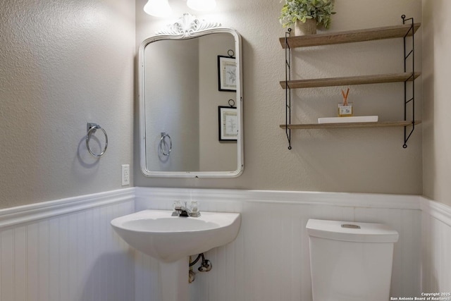 6039 Woodway Ct, San Antonio, TX 78249 - half bathroom featuring wainscoting, toilet, and a decorative wall