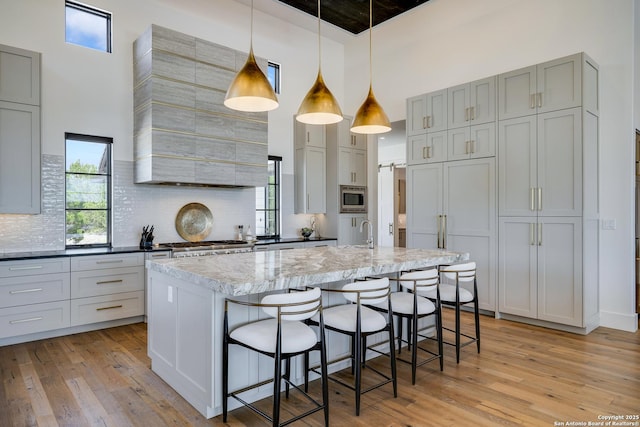 121 Greystone Pt, Boerne, TX 78006 - kitchen featuring a high ceiling, light wood finished floors, stainless steel microwave, backsplash, and light stone counters