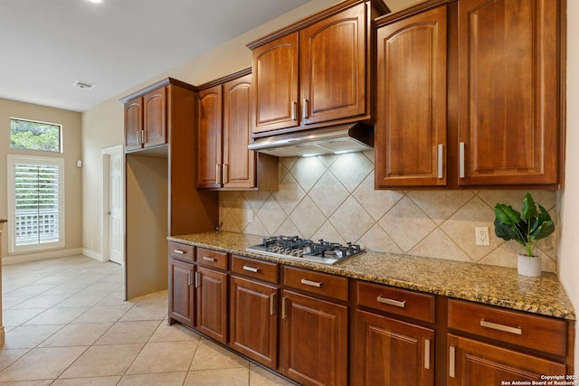 27711 Woodway Bnd, Boerne, TX 78006 - kitchen featuring under cabinet range hood, stainless steel gas stovetop, light stone counters, backsplash, and light tile patterned floors