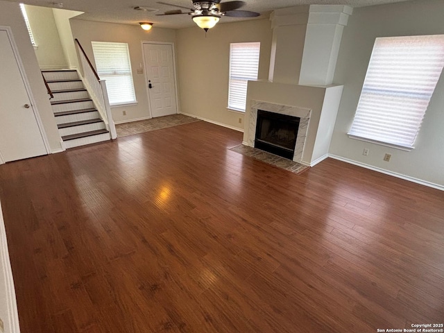 7835 Ruby Mdw, San Antonio, TX 78251 - unfurnished living room featuring ceiling fan, stairway, dark wood-style floors, and a tile fireplace