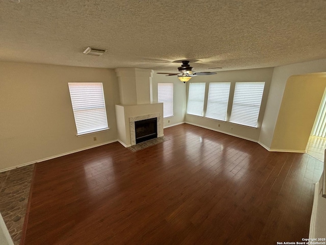 7835 Ruby Mdw, San Antonio, TX 78251 - unfurnished living room with dark wood-style flooring, baseboards, ceiling fan, a tiled fireplace, and a textured ceiling