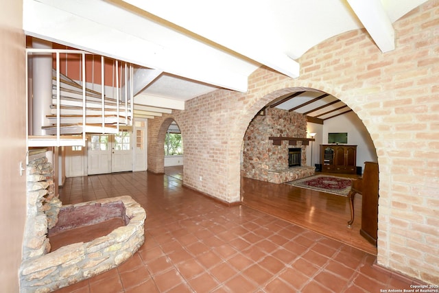 5803 Hollyhock, San Antonio, TX 78240 - unfurnished living room featuring beam ceiling, a stone fireplace, arched walkways, stairway, and brick wall