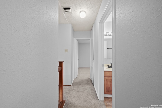 9387 Village Lance, San Antonio, TX 78250 - corridor featuring a textured wall, a textured ceiling, light colored carpet, a sink, and baseboards