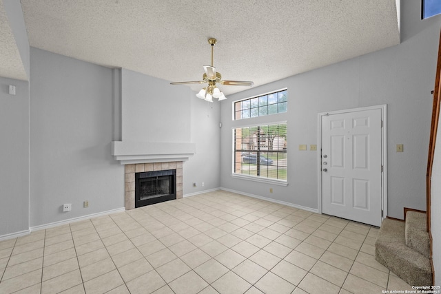 9387 Village Lance, San Antonio, TX 78250 - unfurnished living room with ceiling fan, a textured ceiling, a tiled fireplace, light tile patterned floors, and baseboards