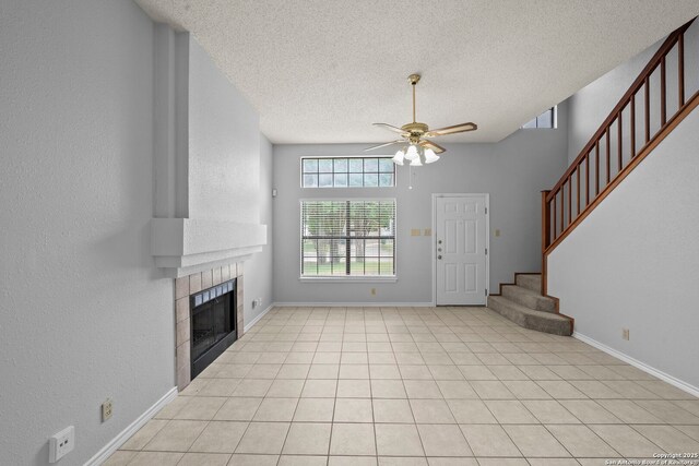 9387 Village Lance, San Antonio, TX 78250 - unfurnished living room featuring ceiling fan, a tile fireplace, a textured ceiling, stairway, and baseboards