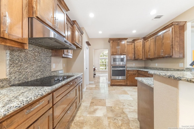 22919 Hightop, Elmendorf, TX 78112 - kitchen with stainless steel appliances, under cabinet range hood, brown cabinets, light stone counters, and decorative backsplash