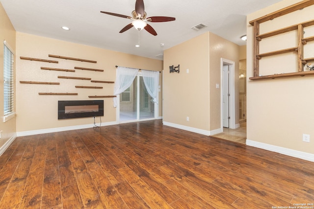 22919 Hightop, Elmendorf, TX 78112 - unfurnished living room with a glass covered fireplace, ceiling fan, wood-type flooring, baseboards, and recessed lighting