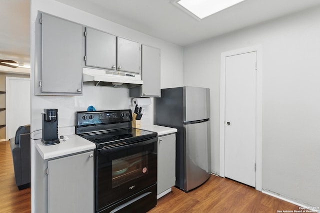 2435 Westgard, San Antonio, TX 78245 - kitchen with black range with electric cooktop, under cabinet range hood, wood finished floors, light countertops, and freestanding refrigerator