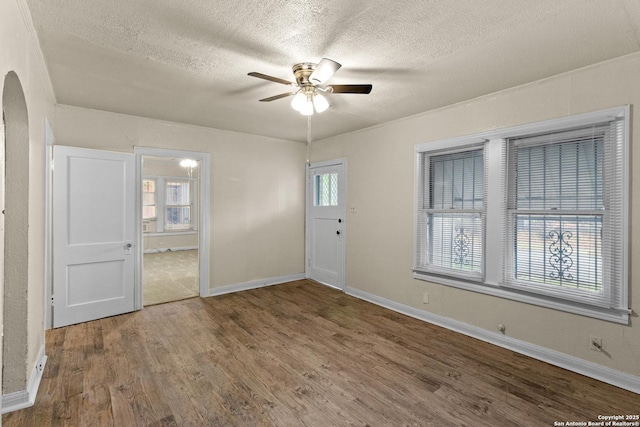 1001 Mason, San Antonio, TX 78208 - unfurnished room with arched walkways, a ceiling fan, a textured ceiling, wood finished floors, and baseboards