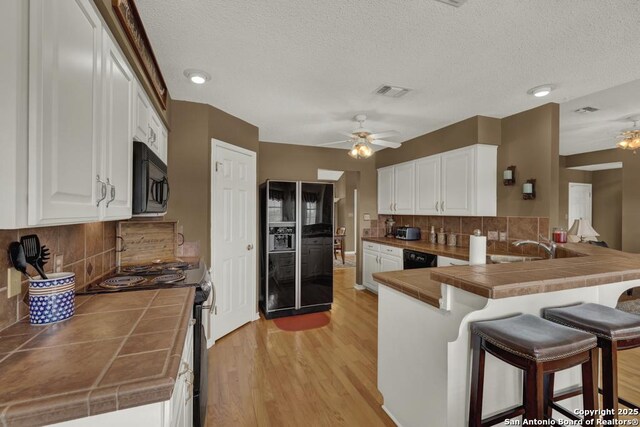 821 Lakeview, Canyon Lake, TX 78133 - kitchen with tile counters, black appliances, a ceiling fan, a peninsula, and a kitchen breakfast bar