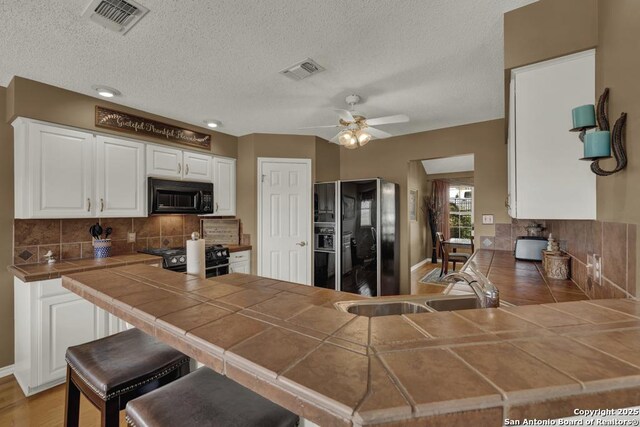 821 Lakeview, Canyon Lake, TX 78133 - kitchen with black appliances, tile countertops, a peninsula, tasteful backsplash, and white cabinetry