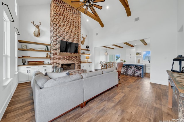 104 Bayberry Ct, La Vernia, TX 78121 - living room with ceiling fan, beamed ceiling, high vaulted ceiling, dark wood-style flooring, and a brick fireplace