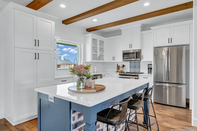 104 Bayberry Ct, La Vernia, TX 78121 - kitchen with appliances with stainless steel finishes, beam ceiling, white cabinetry, glass insert cabinets, and a kitchen bar