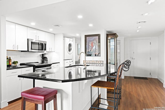 1006 Guadalupe St Unit 1B, Kerrville, TX 78028 - kitchen with appliances with stainless steel finishes, stacked washer / dryer, a breakfast bar, dark wood-type flooring, and dark countertops