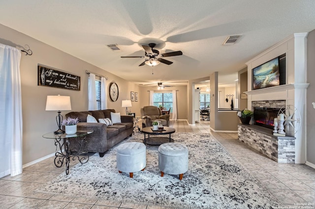 2334 Creekside Bnd, San Antonio, TX 78259 - living room featuring a ceiling fan, a stone fireplace, light tile patterned floors, baseboards, and a textured ceiling