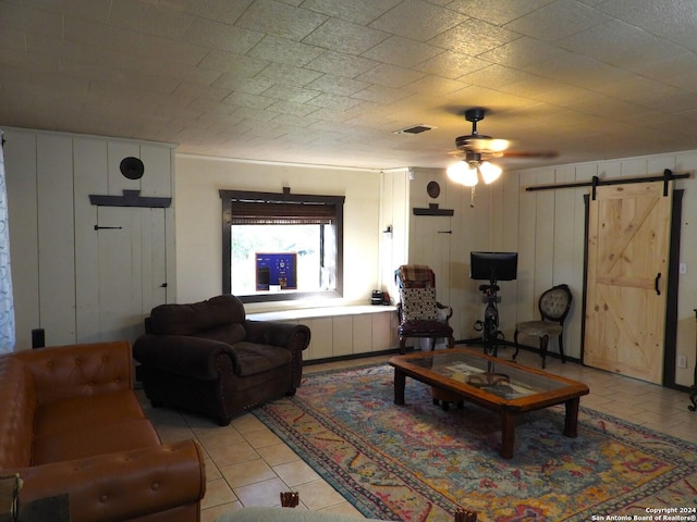 155 Scenic Cir, Lakehills, TX 78063 - living room with a barn door, a ceiling fan, light tile patterned flooring, and wood walls