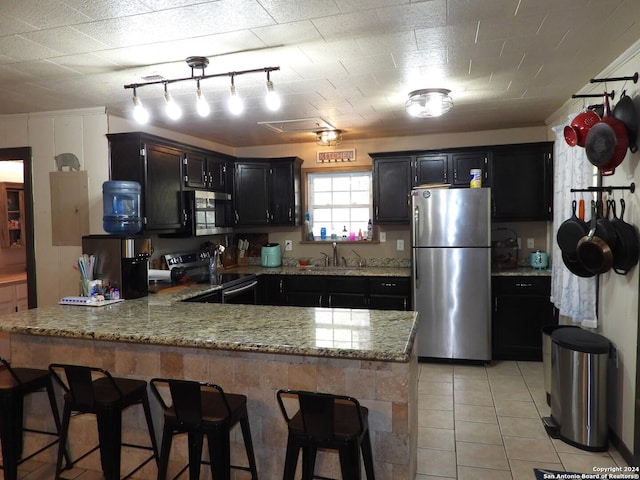 155 Scenic Cir, Lakehills, TX 78063 - kitchen with stainless steel appliances, a peninsula, a sink, dark cabinetry, and light tile patterned floors