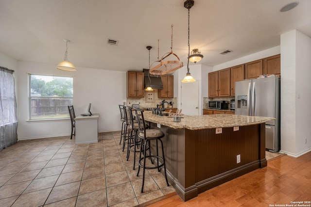 4706 Granite Shls, San Antonio, TX 78244 - kitchen with appliances with stainless steel finishes, custom range hood, a kitchen bar, brown cabinets, and light stone counters