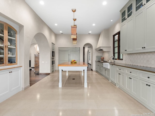 2835 Palomino Spgs, Bandera, TX 78003 - kitchen featuring custom exhaust hood, arched walkways, backsplash, baseboards, and glass insert cabinets