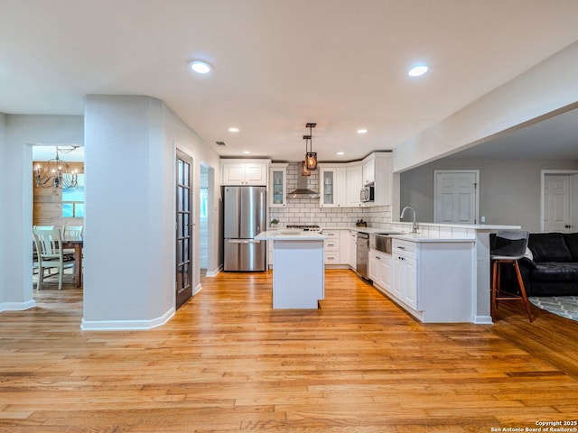 221 Harmon, San Antonio, TX 78209 - kitchen featuring stainless steel appliances, wall chimney exhaust hood, a peninsula, open floor plan, and light wood-style flooring