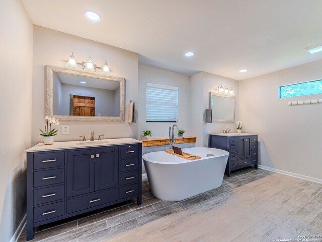 221 Harmon, San Antonio, TX 78209 - bathroom featuring two vanities, a freestanding tub, wood finish floors, recessed lighting, and baseboards