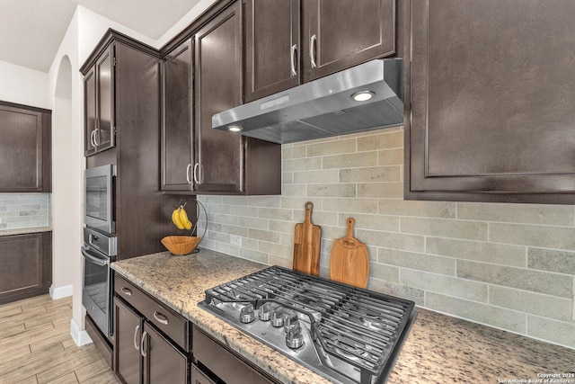 11926 Tower Crk, San Antonio, TX 78253 - kitchen with appliances with stainless steel finishes, under cabinet range hood, arched walkways, backsplash, and light stone countertops