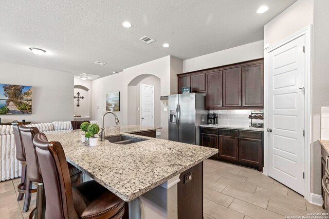 27418 Camellia Trce, Boerne, TX 78015 - kitchen with stainless steel fridge, a kitchen breakfast bar, light stone countertops, arched walkways, and dark brown cabinetry