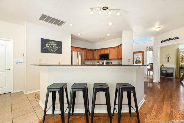 9106 Thomas York, San Antonio, TX 78251 - kitchen featuring black microwave, freestanding refrigerator, brown cabinetry, a breakfast bar, and dark countertops