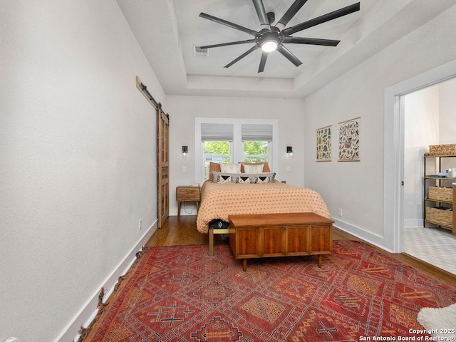 211 W High Ave, San Antonio, TX 78210 - bedroom featuring a barn door, a raised ceiling, baseboards, and wood finished floors