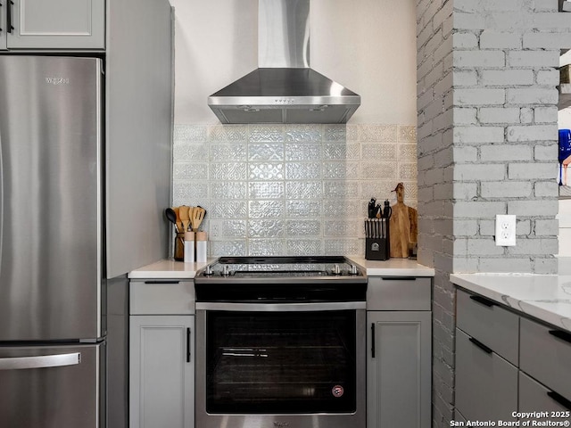 211 W High Ave, San Antonio, TX 78210 - kitchen with wall chimney exhaust hood, appliances with stainless steel finishes, decorative backsplash, light stone counters, and gray cabinets